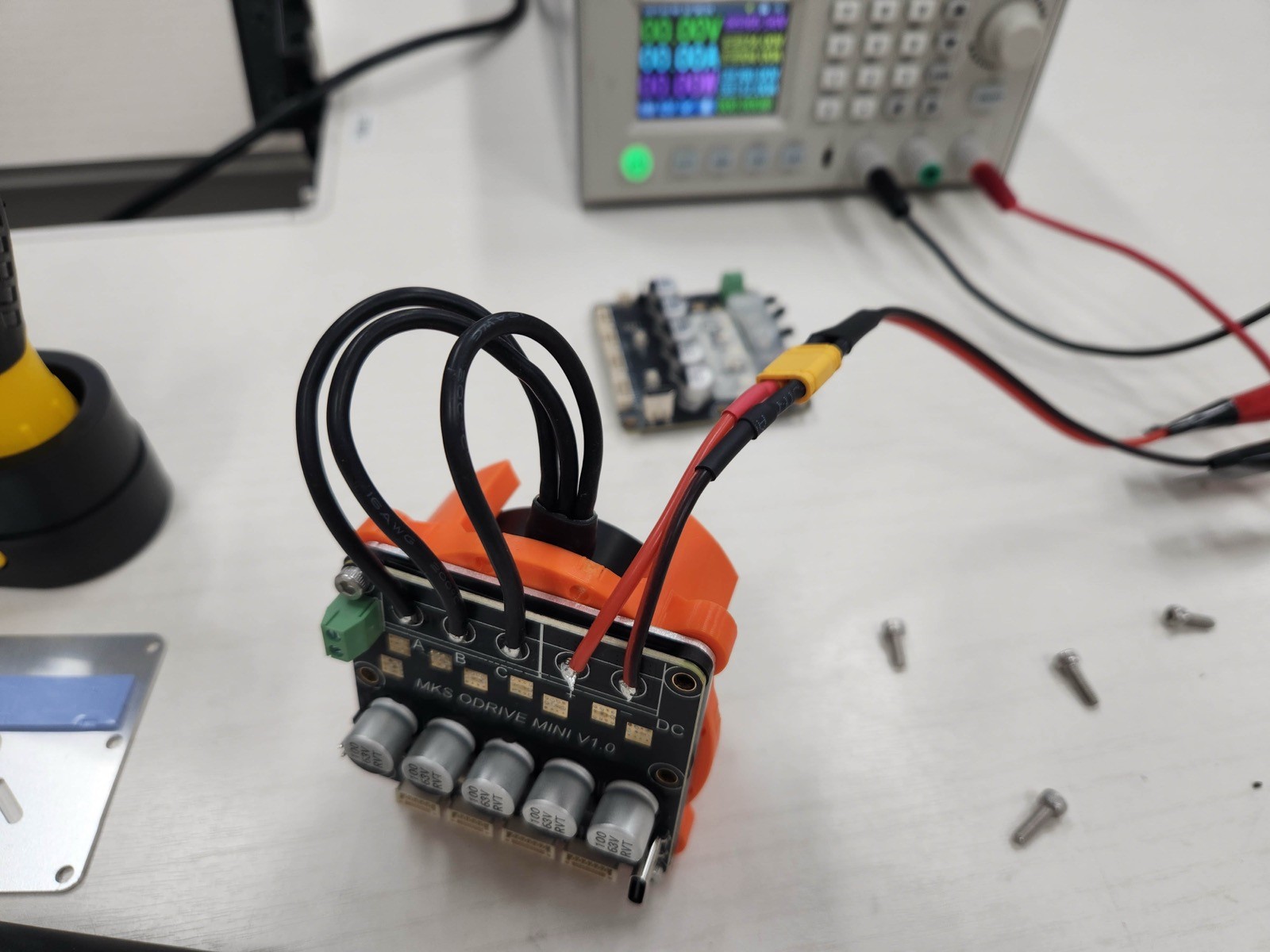 Angled view of an assembled actuator with motor and power wires soldered directly to the driver board, connected to a bench power supply.