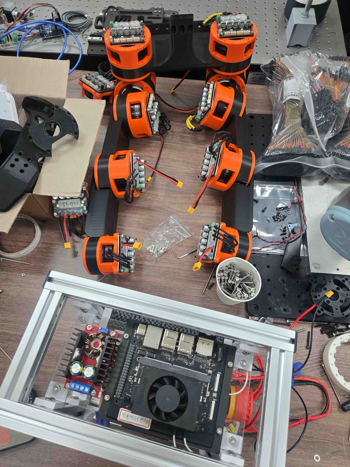 Top view of both assembled legs laid out on a workbench, with the body frame in front showing the 12 V to 24 V booster, the computer, and the emergency stop button.